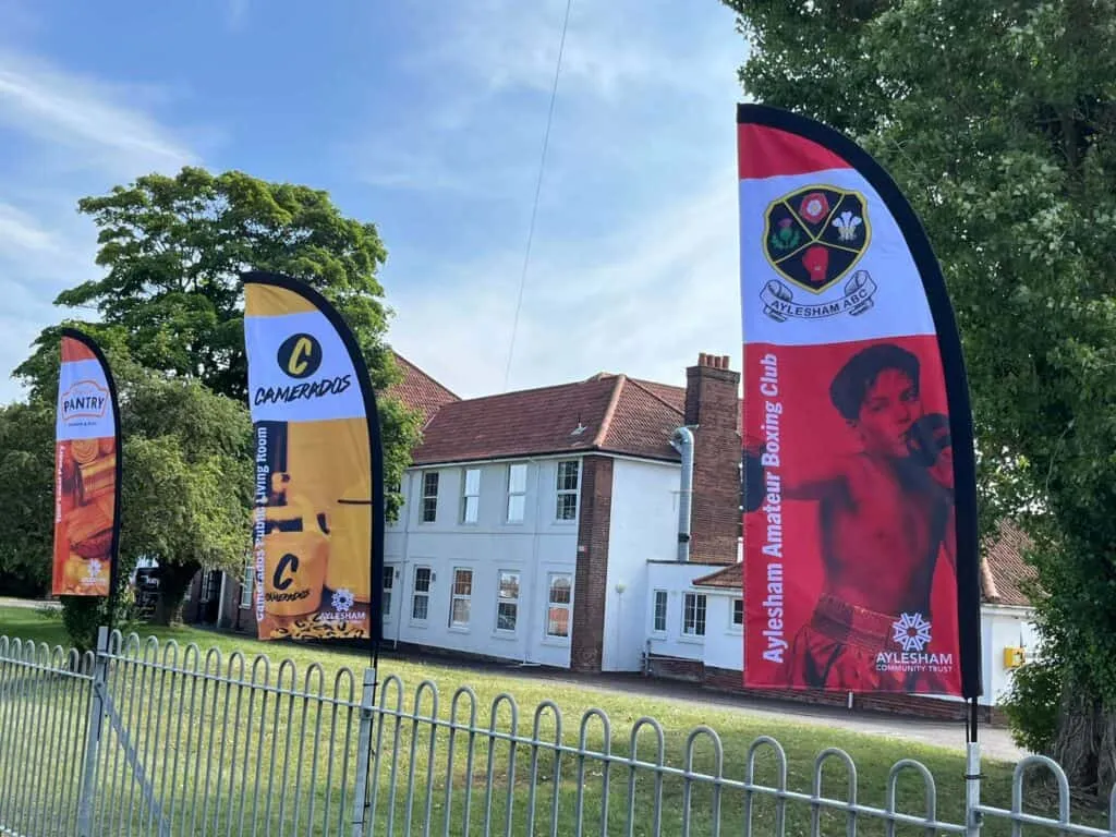 Bright promotional flags outside Aylesham Community Trust showcasing local boxing, community groups, and food programs, highlighting community engagement and youth sports initiatives in Aylesham.