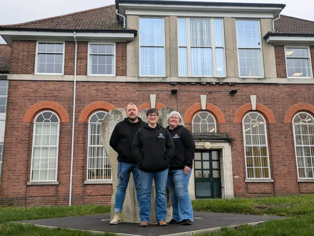 Empowered community volunteers standing outside Aylesham Community Trust building in front of a large brick structure with tall windows.